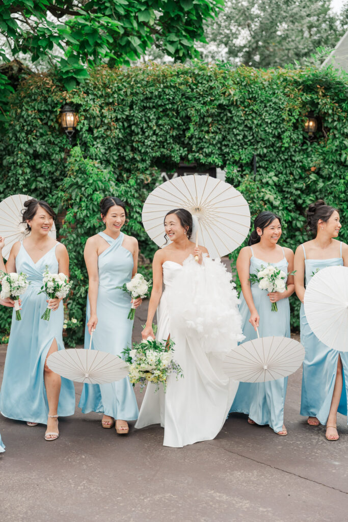 Stephanie and her bridesmaids holding white parasols in the Gatehouse gardens