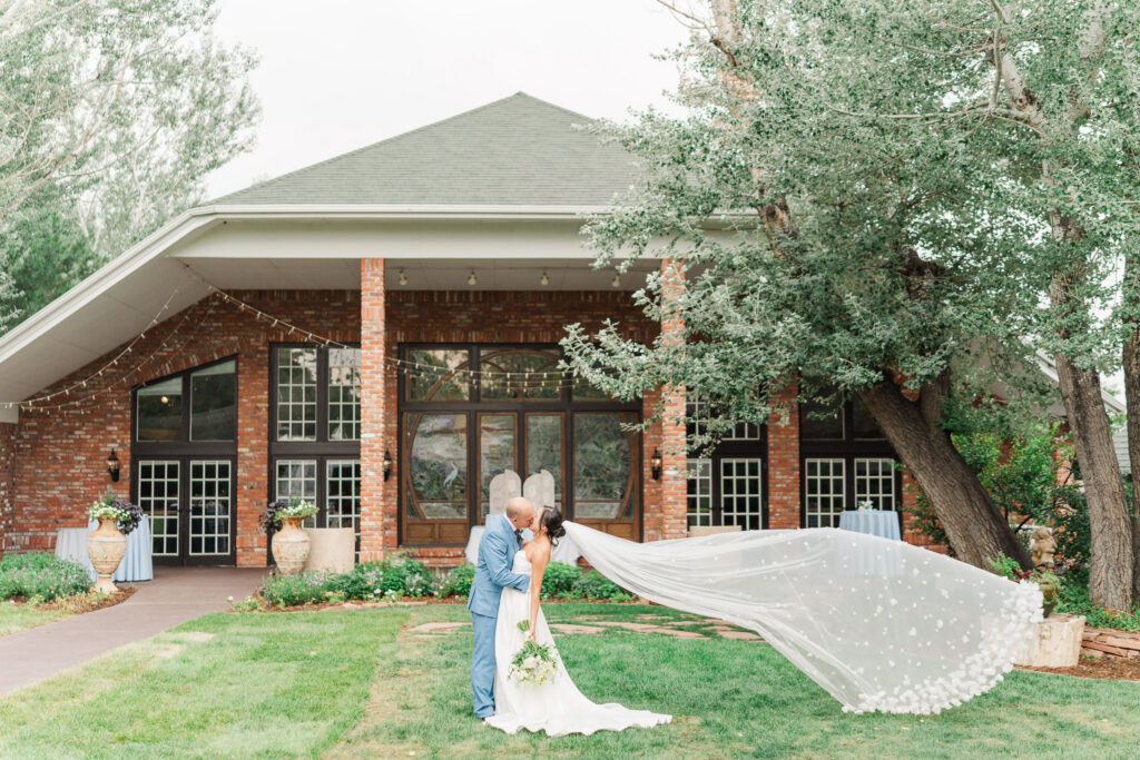 Stephanie and Sam outside The Gatehouse with her veil flowing across the lawn