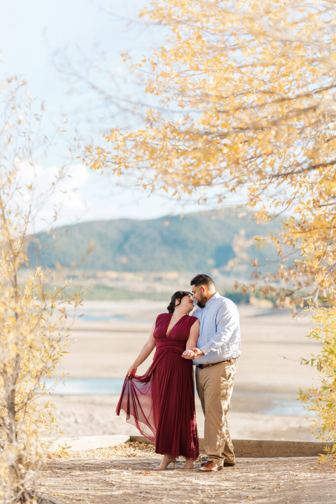 Cathie and Jesse hold hands beneath golden aspens with Lake Dillon and the mountains behind them.